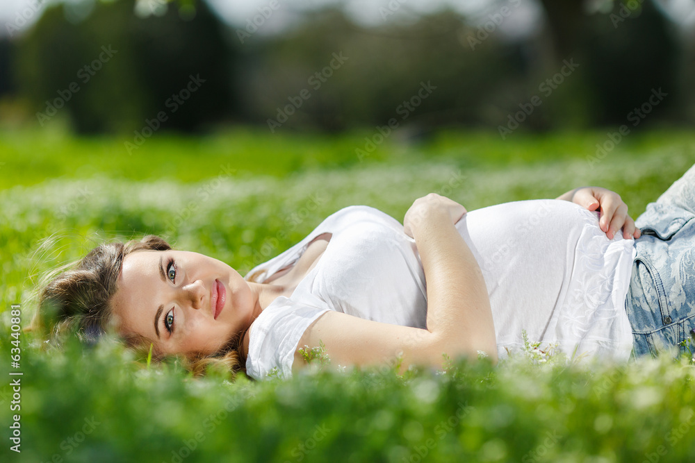 Portrait of a pregnant woman lying on green grass in the park Portrait of a pregnant woman lying on green grass in the park