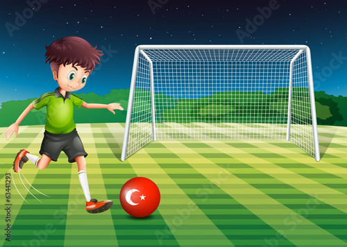 A boy kicking the ball at the field with the flag of Turkey