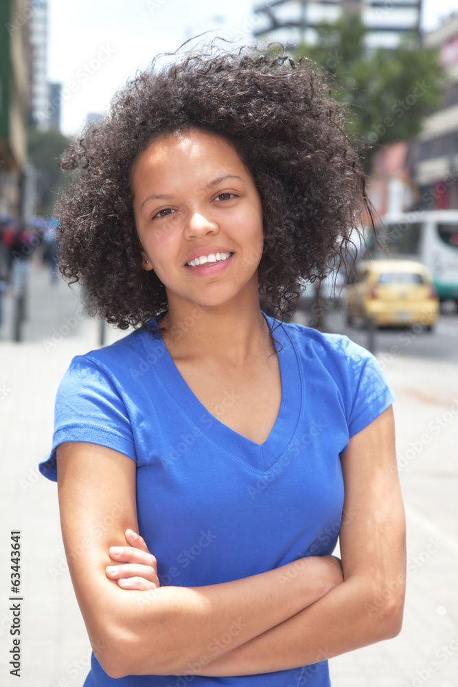Fototapeta premium Attractive woman with curly hair and crossed arms in the city