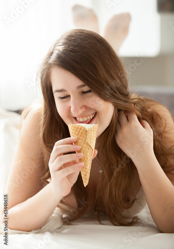 Smiling brunette woman eating ice cream at bedroom