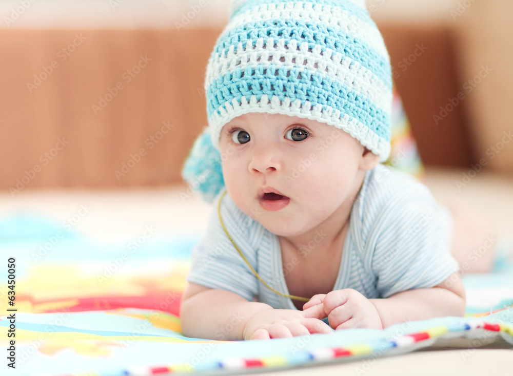 little child lying on a children's rug in the white-blue cap. little child lying on a children's rug in the white-blue cap.