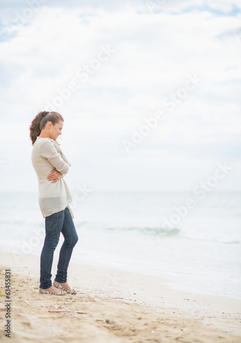 Thoughtful young woman standing on cold beach © Alliance