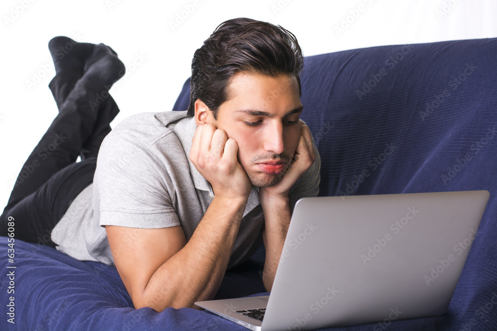 Disappointed or bored young man staring at laptop PC Disappointed or bored young man staring at laptop PC