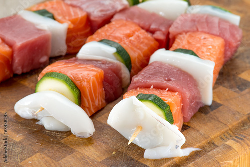 Spiedini di pesce misto crudi posti su un tagliere di legno photo