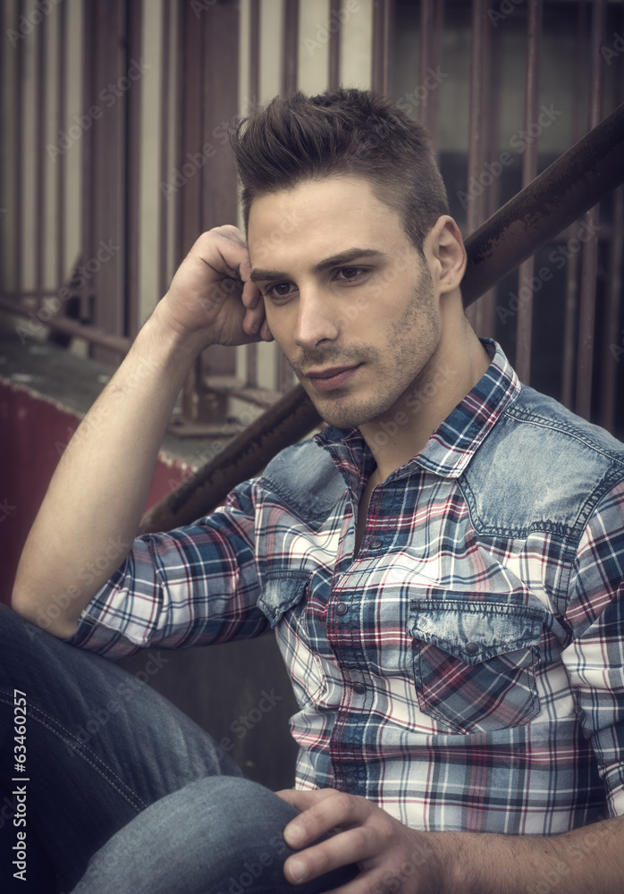 Sad, serious young man sitting and looking away Sad, serious young man sitting and looking away