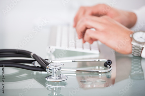 View of stethoscope with doctor using computer keyboard