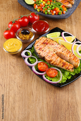 Tasty grilled salmon with lemon and vegetables, on wooden table