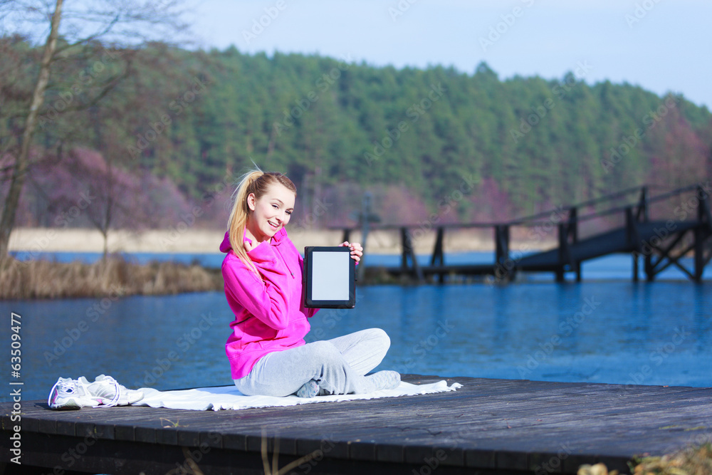 Woman teenage girl in tracksuit showing tablet on pier outdoor