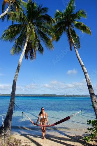 Young woman in bikini standing by the hammock between palm trees