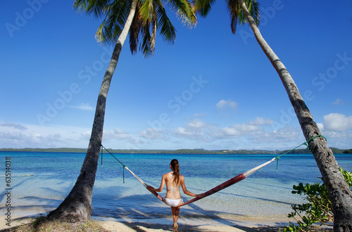 Young woman in bikini sitting in a hammock between palm trees, O photo