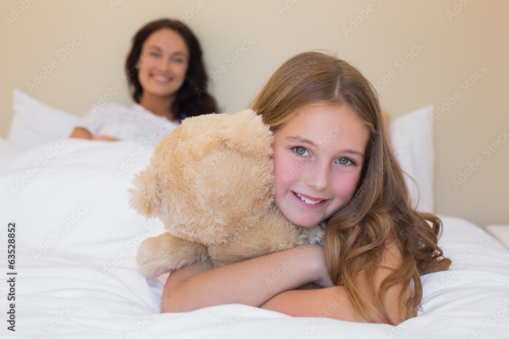 Girl embracing teddy bear with mother in background Girl embracing teddy bear with mother in background