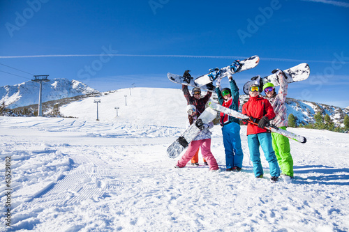 Five friends holding snowboards and skies together