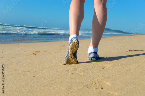 Woman runner legs in shoes on beach, running concept