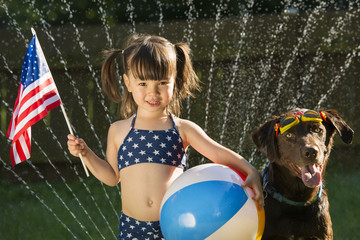 Preschooler holding US flag and beachball posing with dog