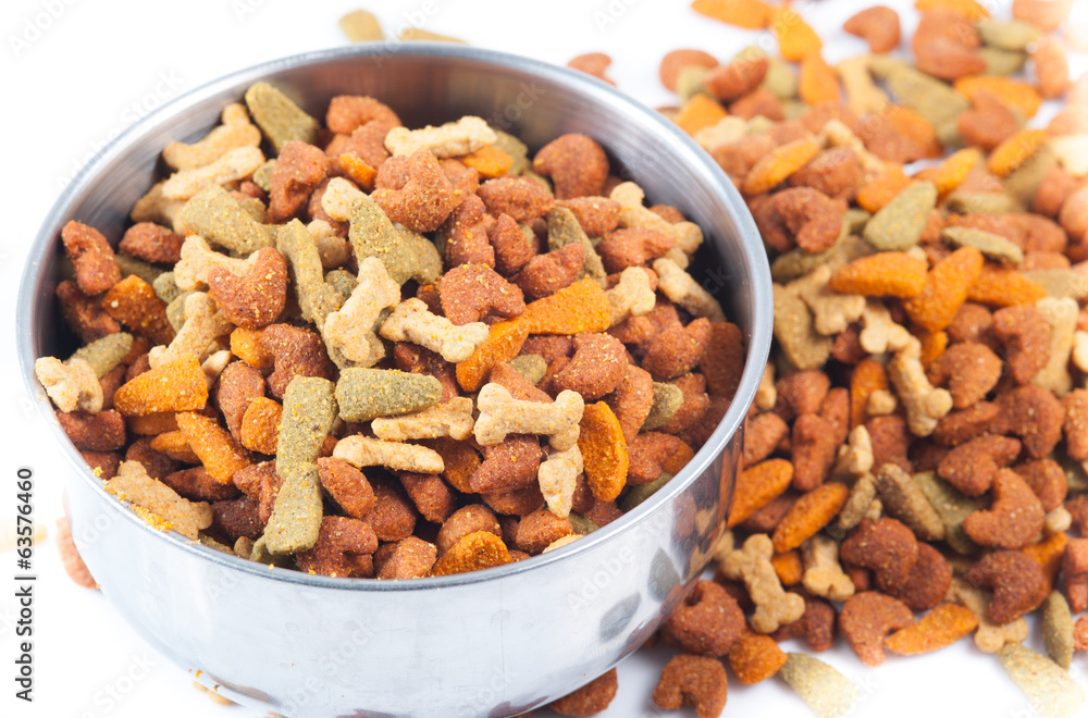 Silver bowl full and overflowing with dog food bits on a white b Silver bowl full and overflowing with dog food bits on a white b