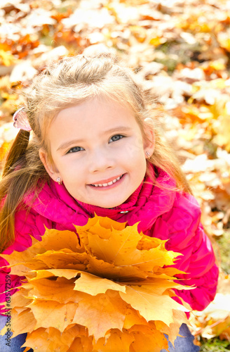 Autumn portrait of cute smiling little girl with maple leaves