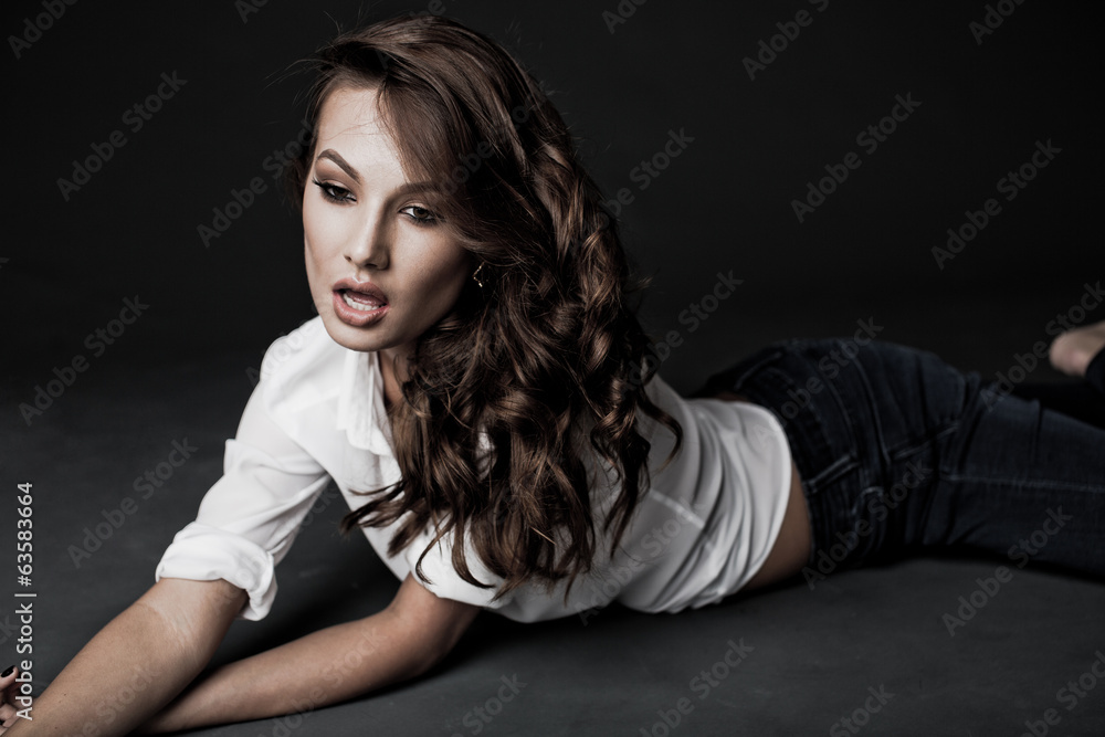 Naklejka premium Lovely woman in white blouse and blue jeans lying on the floor