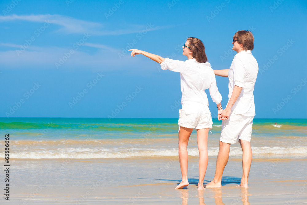 Young happy caucasian couple in white standing on beach looking Young happy caucasian couple in white standing on beach looking