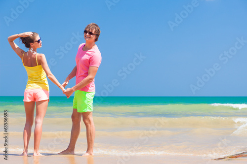 Couple in bright clothes holding hands on tropical beach.