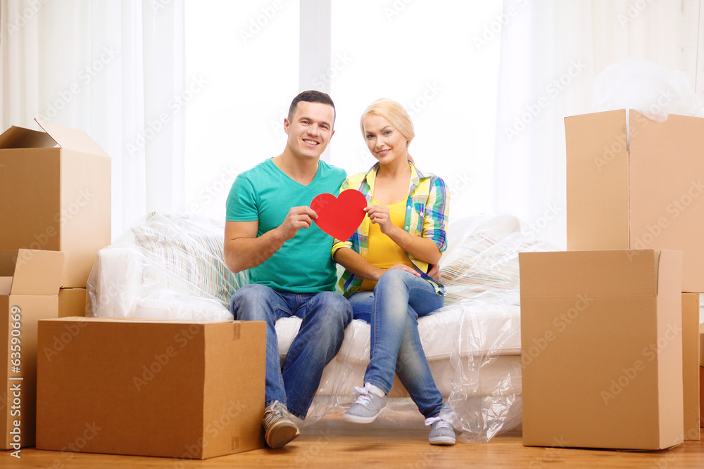 smiling couple with red heart on sofa in new home smiling couple with red heart on sofa in new home