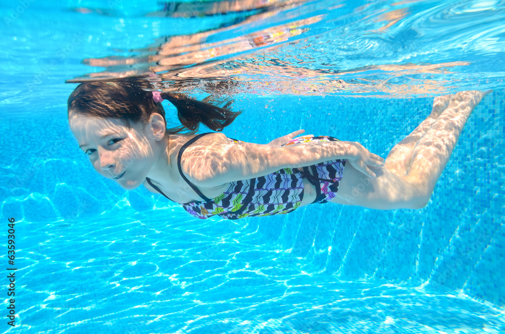 Happy active underwater child swims in pool, girl swimming