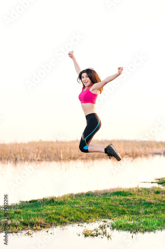 sports woman near lake on sunset jumping in the air