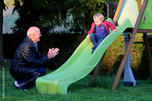 Happy grandfather plays with his granddaughter on the slide