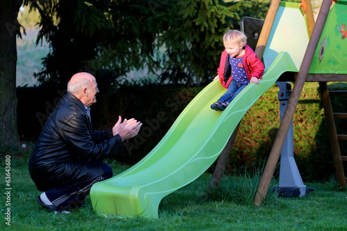 Happy grandfather plays with his granddaughter on the slide