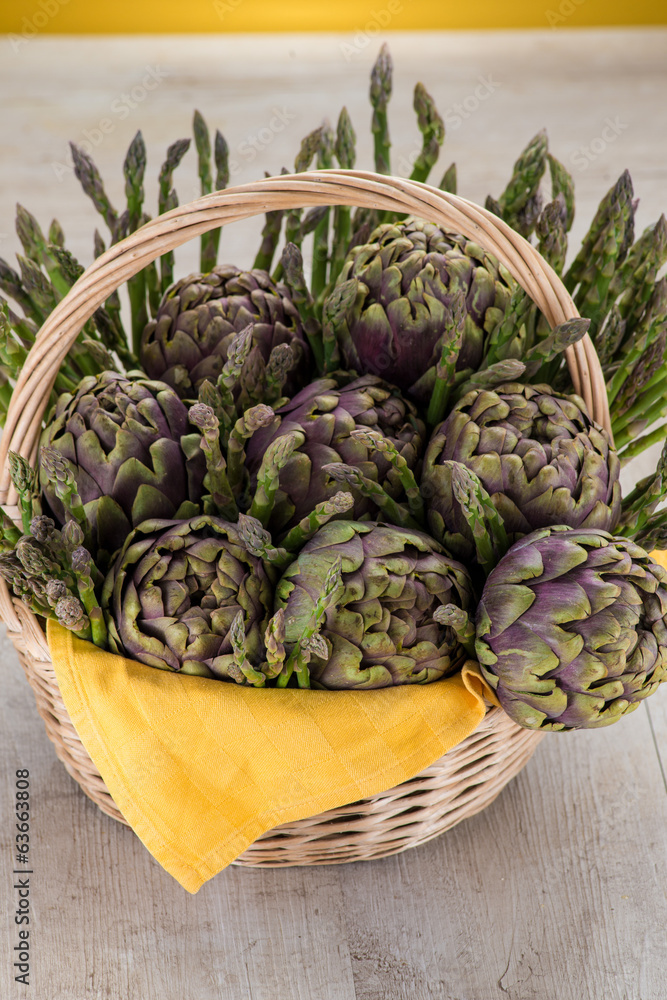 Obraz premium Cestino di vimini con carciofi ed asparagi su un tavolo