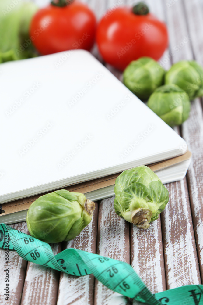 Notebook with measuring tape and vegetables on wooden Notebook with measuring tape and vegetables on wooden