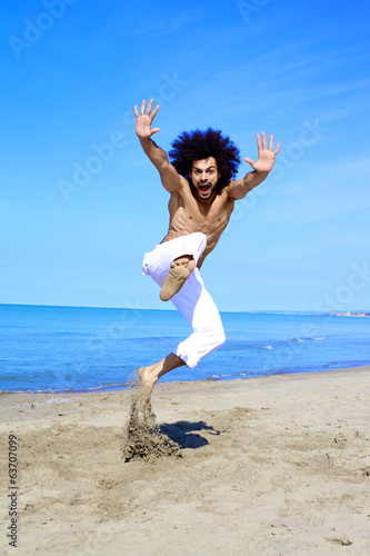 Man having fun jumping on sand in front of the ocean in vacation