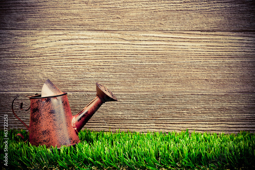 old and rusty watering can on green grass with wood background photo