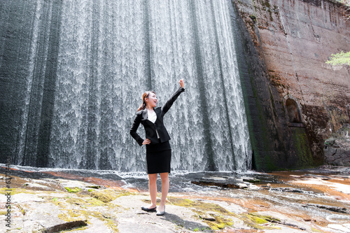 滝の前に立つアジアのスーツの女性