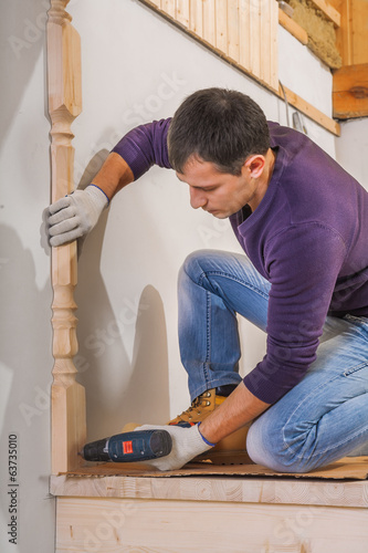 young carpenter fixing wooden post with cordless drill