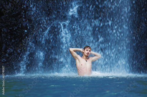 Handsome young man refreshing in waterfall in bali