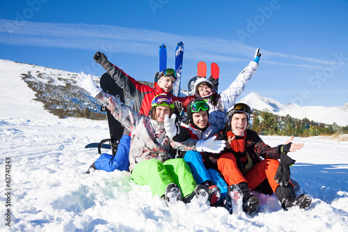 Sitting friends with snowboards lifting hands up