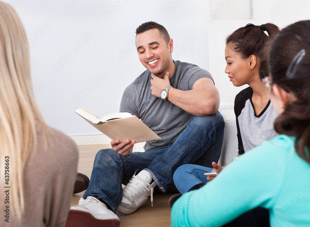 Group of college students reading book on floor Group of college students reading book on floor