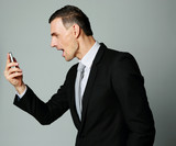 Angry businessman yelling on his cell phone on gray background