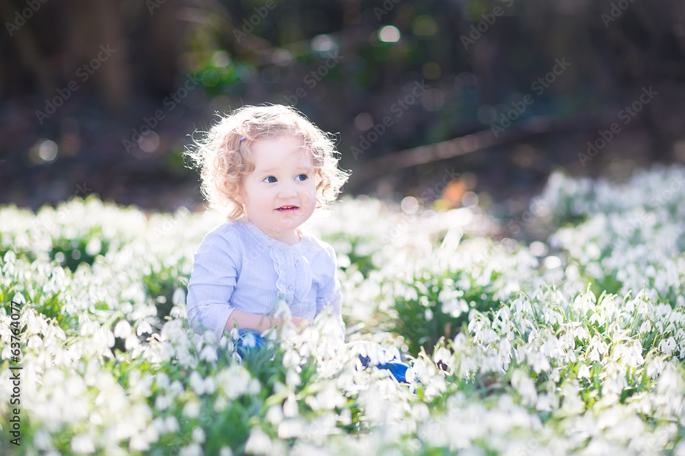 Adorable curly toddler girl playing with first spring flowers Adorable curly toddler girl playing with first spring flowers