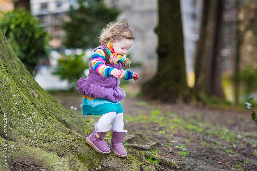 Cute toddler girl playing at a big tree in a spring park Cute toddler girl playing at a big tree in a spring park