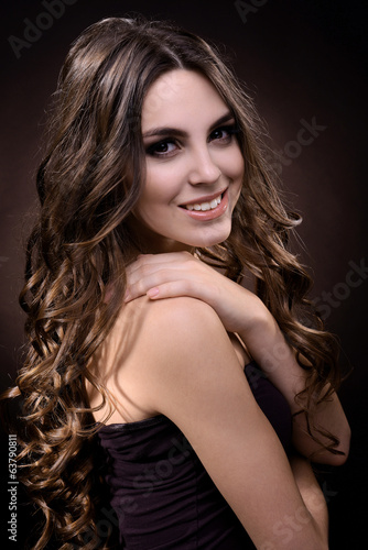 Beautiful young woman with long hair on dark brown background