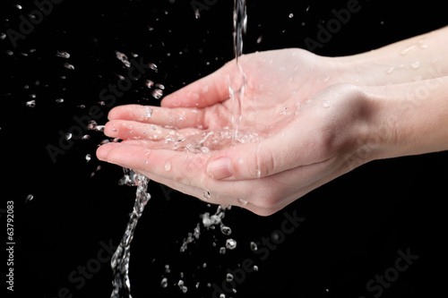 Human hands with water splashing on them on black background