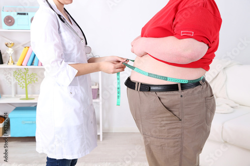 Doctor examining  patient obesity on light background photo