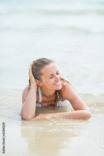 Happy young woman in swimsuit laying on sea shore