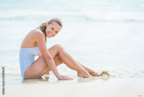 Happy young woman in swimsuit sitting on sea coast