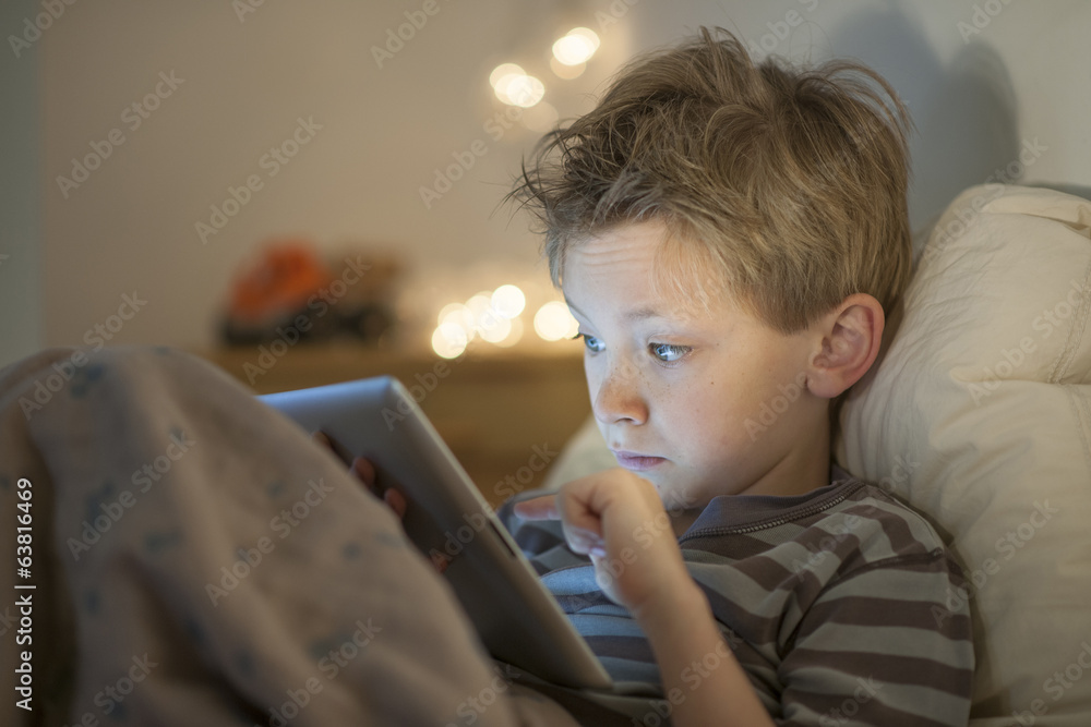 little boy at expressive face using a digital tablet in bed little boy at expressive face using a digital tablet in bed