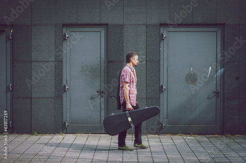 Man in short sleeve shirt walking with guitar case