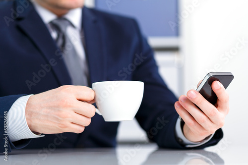 Businessman holding a mobile phone and coffee