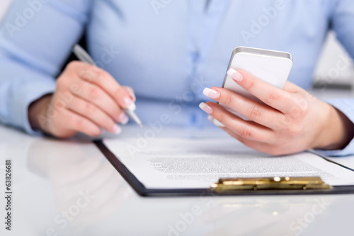 Young woman working with a mobile phone and holding a pen