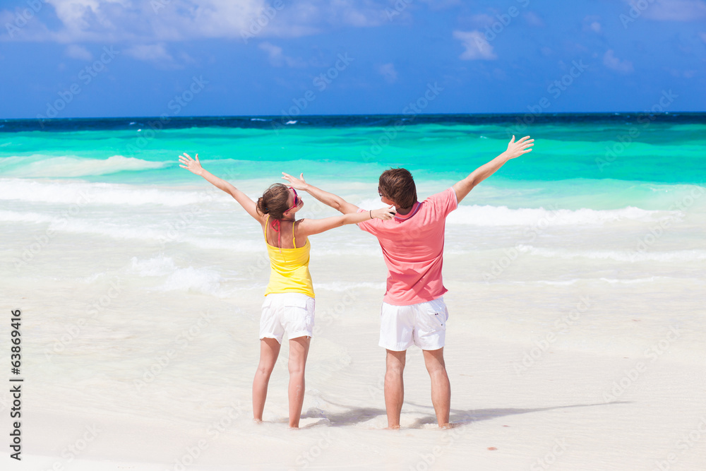back view of couple waving hands on tropical beach